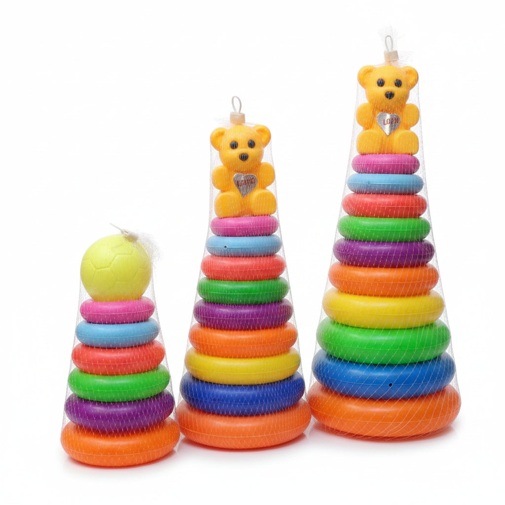 Three colorful plastic stacking toys wrapped in mesh, displayed on a glass counter in a toy store. The set includes a soccer ball stacker on the left, a yellow teddy bear stacker in the center, and a rainbow ring stacker on the right.