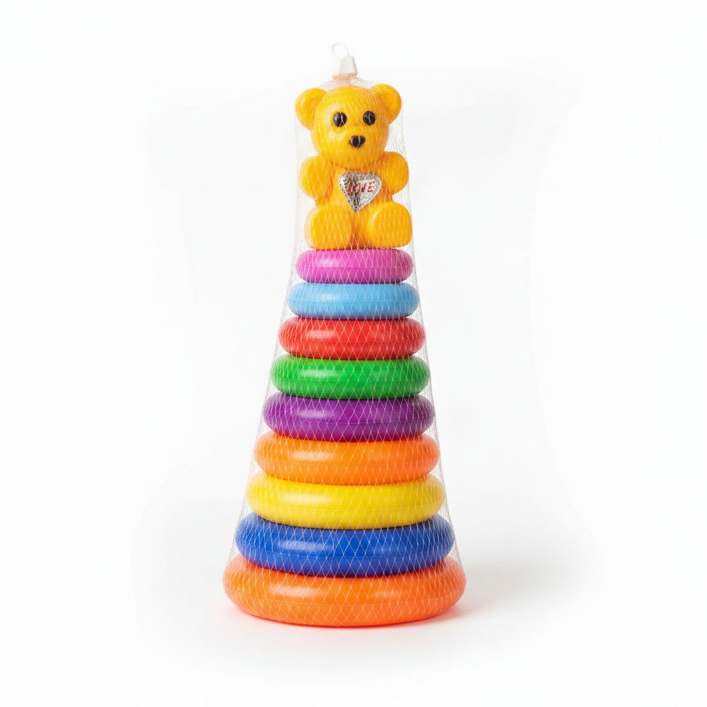 A colorful stacking ring toy with a yellow teddy bear at the top, packaged in a clear mesh bag and displayed on a glass counter in a toy store.